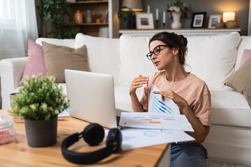 Young business woman working at home in home office sitting on floor of her apartment, work on laptop computer financial calculations. Female freelance worker using technology for global business.