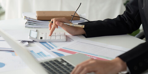 Business Professional Using Calculator and Laptop for Financial Analysis in Office Environment