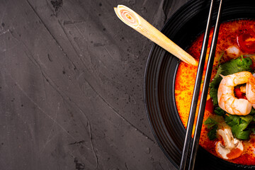 tom yum kung Spicy Thai soup with shrimp in a black bowl on a dark stone background, top view, copy space