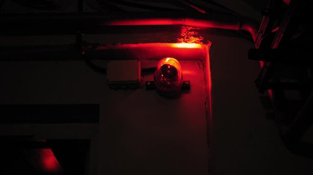 Close-up of a rotating red emergency siren lamp on the wall of a dark tunnel. A bomb shelter, an emergency signal on the wall during an air raid.
