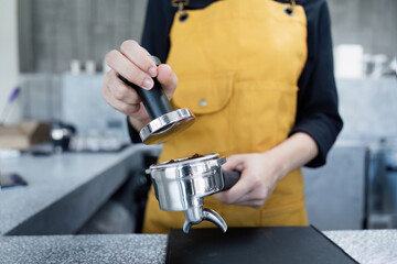 Barista Preparing Espresso with Tamper in Modern Coffee Shop Wearing Yellow Apron