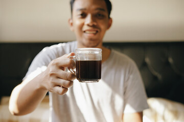 Asian man enjoy drinking coffee on the bed after wake up from sleep