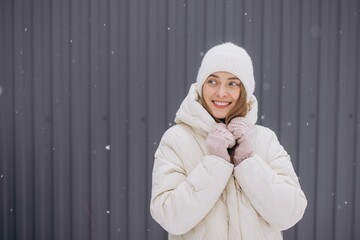 A happy woman in knitted mittens poses against a background of a gray wall in winter