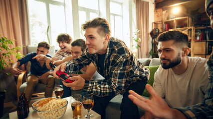 Victory and defeat shared among friends, but good vibes stay strong. Drinks and banter fuel this evening of lighthearted competition. Concept of football fans, sport evens, video games and cybersport.