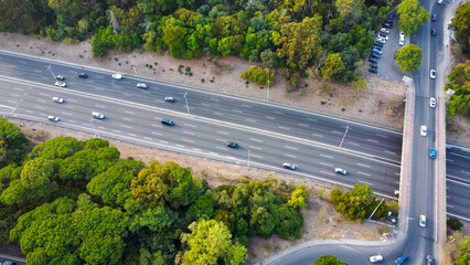 Autoestrada em Monsanto, Lisboa, ao pôr do sol com tráfego em movimento. O céu alaranjado ilumina a estrada e os veículos, criando um contraste entre a natureza e a paisagem urbana.