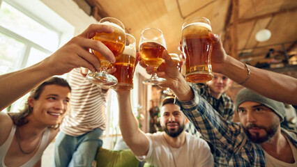 Celebration hits high as all guys raise their glasses for victory toast. Table full of snacks and drinks testament to fun they're having. Concept of football fans, sport evens, video games, cybersport