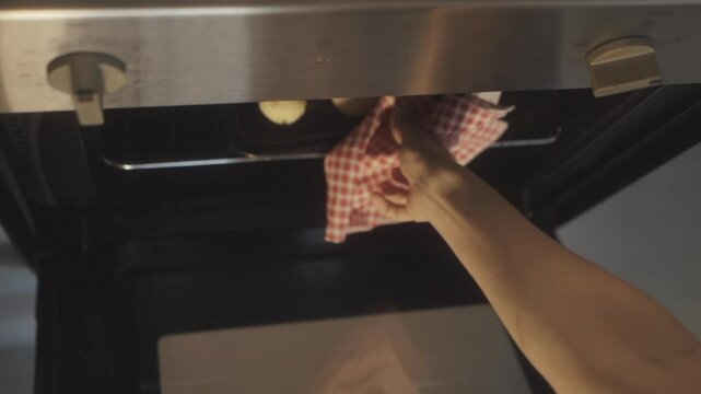 Carefully taking out freshly baked chipa bread from the oven, showcasing a traditional snack made at home. Warm, golden brown bread rolls, a delicious treat in northeastern argentiniean tradition