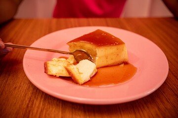 Person eating flan on a pink plate.