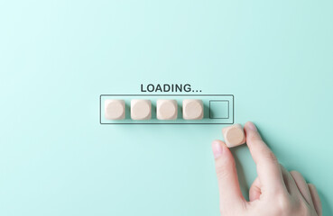 Loading bar concept. Progress bar, A hand placing a wooden block into a loading bar made of blocks, set against a mint green background, representing progress, patience, update, or waiting.