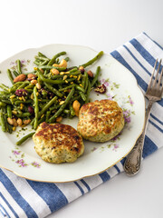 Delicious green bean salad paired with savory fish cakes on a floral plate, artfully arranged with a blue striped napkin