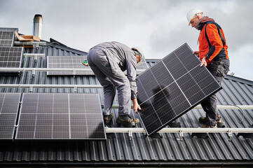 Engineers building solar panel system on roof of house. Men workers in helmets carrying...