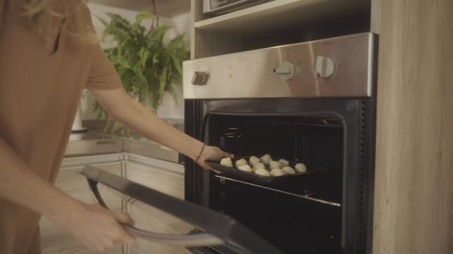 Person baking traditional chipa bread at home, placing a tray of dough balls into the oven in a warm, inviting kitchen environment