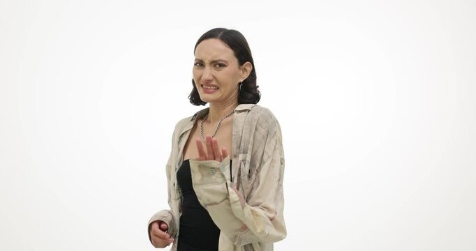 Young woman expresses disgust covering face with hand on white background. Brunette female demonstrates aversion with unpleasant smell slow motion