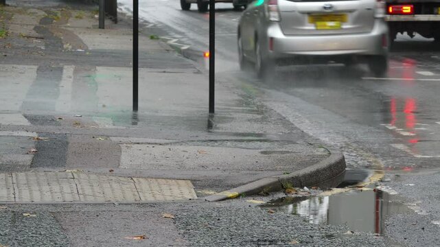 Car splashing through a kerbside puddle.
UK pavement getting splashed by a passing car driving though a puddle.