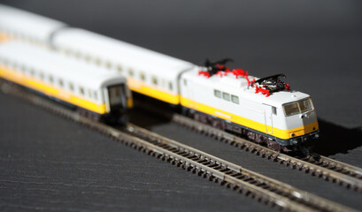 Obraz premium Toy passenger train and railroad with selective focus effect. Model of a locomotive on a dark background.