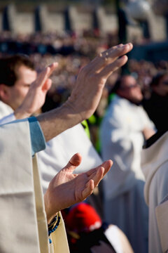 Individuals with raised hands partaking in a religious or spiritual ceremony, amidst a gathering of people, reflecting a communal and spiritual atmosphere.