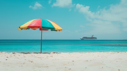 A colorful beach umbrella provides shade on a sandy beach with a calming turquoise sea and a distant cruise ship under a clear blue sky.