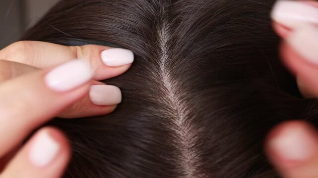 Female hands touching and parting her hair revealing hair loss or thinning hair close up