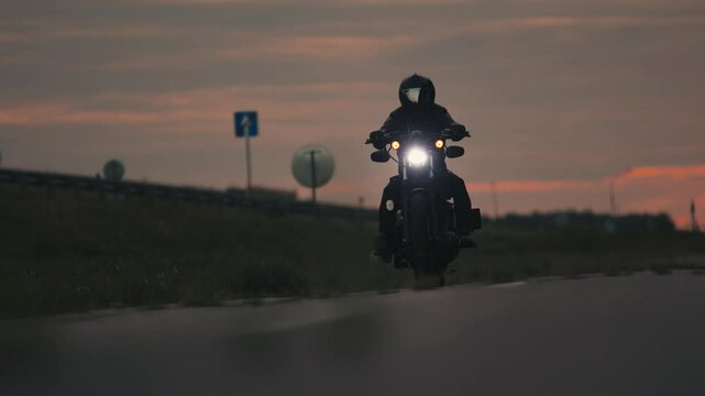 Biker in black helmet rides along highway on motorcycle at sunset evening. Slow motion. Riding on motorcycle requires extreme concentration, prudence and quick reaction