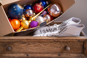 vintage wooden drawer with white ice skates and cardboard box filled with nostalgic colorful Christmas ornaments, holiday season
