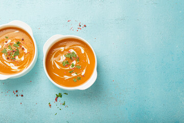 Creamy pumpkin soup bowls on blue background with parsley and pink pepper, a cozy autumn meal option. Space for text