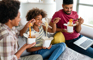 Happy african american family eating on couch with cardboard boxes in living room interior