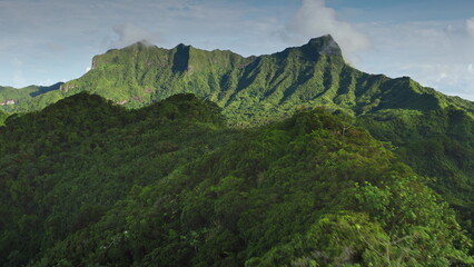 Aerial flight over tropical Bora Bora island green lush rainforest mountain. Mount Otemanu range edge under clouds blue sky. Remote wild nature , exotic summer travel. Drone shot natural background