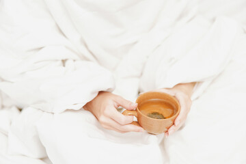 Person sitting in bed with coffee, wrapped in blanket and wearing white robe