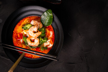tom yum kung Spicy Thai soup with shrimp in a black bowl on a dark stone background, top view, copy space