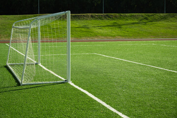 Empty soccer goal on field with artificial green grass. Summer outdoor game.