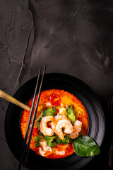 tom yum kung Spicy Thai soup with shrimp in a black bowl on a dark stone background, top view, copy space