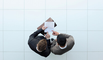 Two businessman signing an agreement. One hand holds the document and the other signs.
