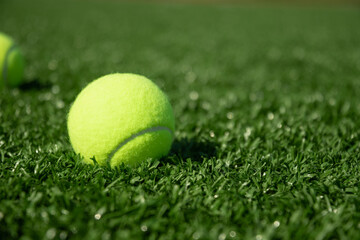 Yellow tennis ball on green sports ground with artificial grass covering. Close up. Copy space. Healthy lifestyle concept.