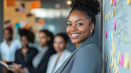 African woman stands in a conference room in a professional workplace, looking at the camera with a smile. Mature business woman preparing to join her colleagues in a meeting. Commercial presentation