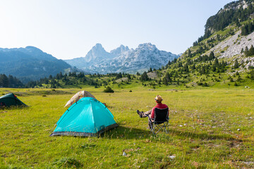 Hiker sitting next to a tent on a mountain in a beautiful valley with a view of rocky peaks in the background