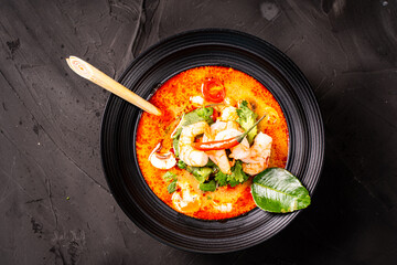 tom yum kung Spicy Thai soup with shrimp in a black bowl on a dark stone background, top view, copy space