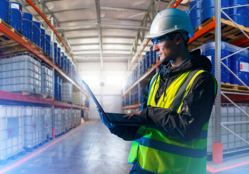 Supervisor at warehouse. Man with laptop in storage area of a manufactory. Production warehouse supervisor. Man manager near racks with barrels and IBC. Supervise uses warehouse software