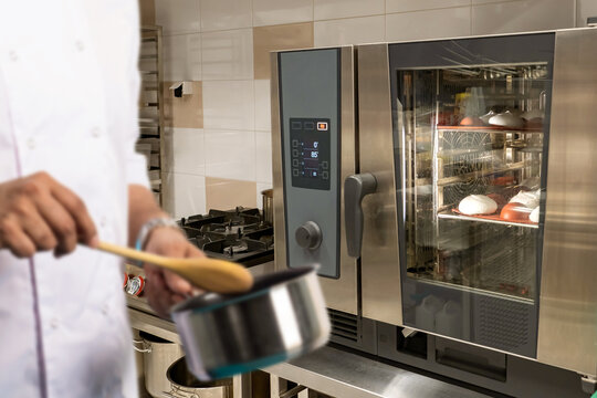 Confectionery shop restaurant. Production desserts. Cakes are baked in oven. Pastry chef hands with saucepan. Bakery employee prepares delicious desserts. Confectionery shop with combi oven