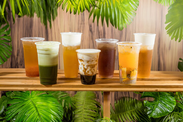 taiwan style boba Iced coffee drinks in plastic cups on wooden shelf with tropical leaves background