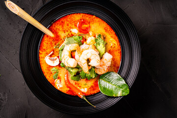 tom yum kung Spicy Thai soup with shrimp in a black bowl on a dark stone background, top view, copy space