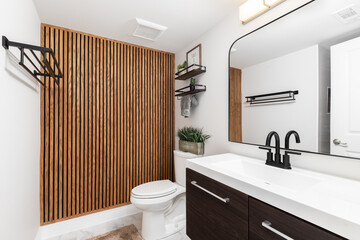 A bathroom with a dark wood cabinet, floating shelves with decorations above the toilet, and a wood slat accent wall.