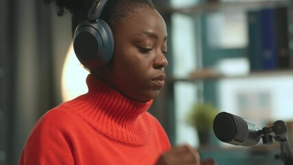 Footage of attractive female radio host wearing headphones while sitting at microphone at work. African American woman enjoying music in professional recording studio. Working day. Parallax effect