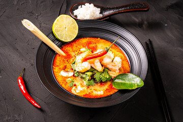 tom yum kung Spicy Thai soup with shrimp in a black bowl on a dark stone background, top view, copy space