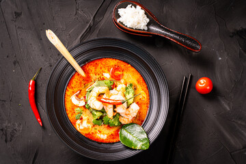tom yum kung Spicy Thai soup with shrimp in a black bowl on a dark stone background, top view, copy space