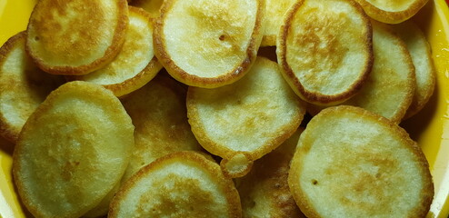 Ruddy fluffy bread pancakes (fritters) in a deep yellow plate (macro, top view, background for tea).
