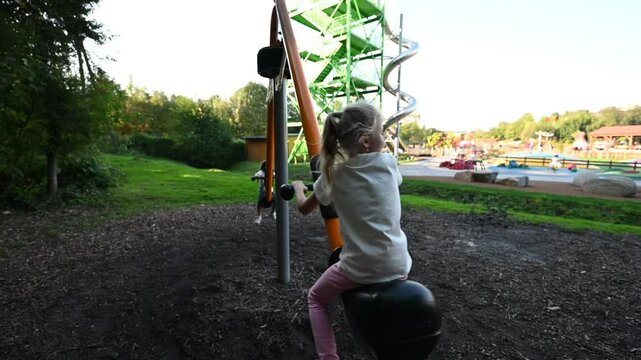 Two young girls enjoy riding a seesaw together on a sunny day. The video shows them laughing and having fun at the park.