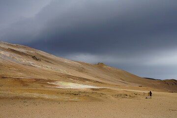 Námafjall Hverir, Reykjahlíð, Iceland - landscape of geothermal zone and tourist sightseeing location with a couple of photographers standing in the otherworldly area