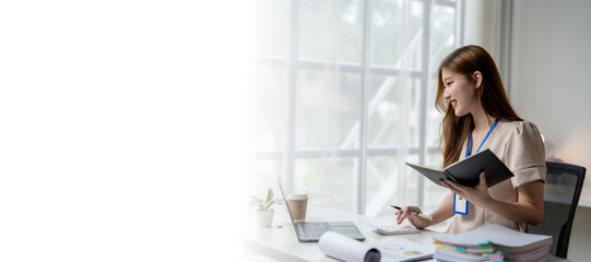 A woman is sitting at a desk with a laptop and a book