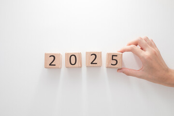 A hand arranging wooden blocks to display the year 2025 on a clean white background.