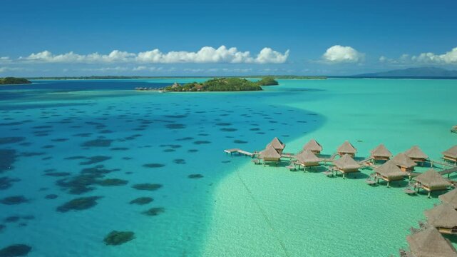 Overwater bungalows huts on tropical island in Bora Bora, crystal clear turquoise coral reef. French Polynesia popular tourist destination. Remote wild nature, exotic summer luxury travel. Aerial view